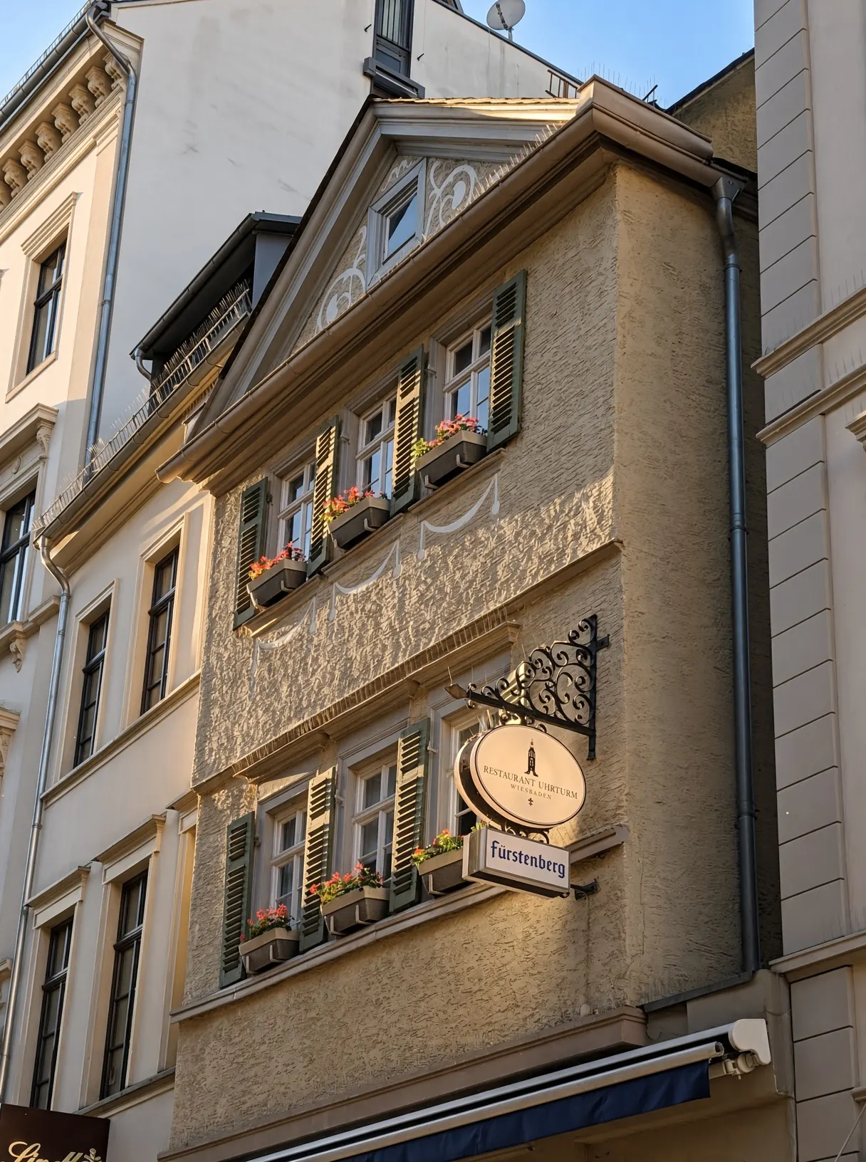 Hausfassade mit grünen Fensterläden, Blumenkästen und dem ovalen Schild Restaurant Uhrturm Wiesbaden